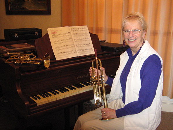 Lynda sitting at a piano holding a trumpet